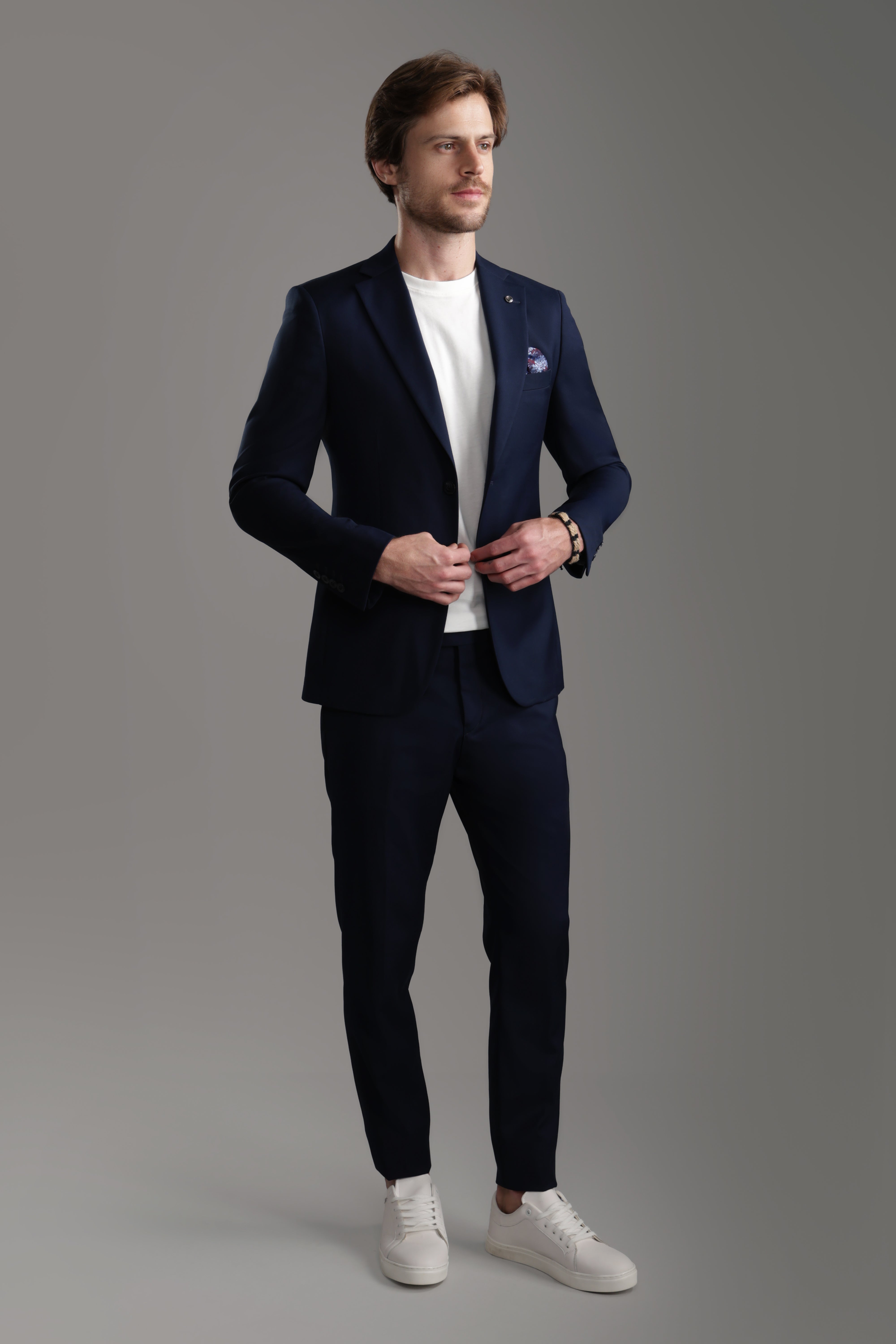 Man in a tailored navy suit with a white t-shirt and sneakers, showcasing a modern formal look.